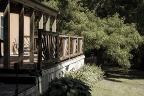 Une terrasse en bois dotée d’une rambarde, entourée d’une végétation luxuriante et d’arbres.