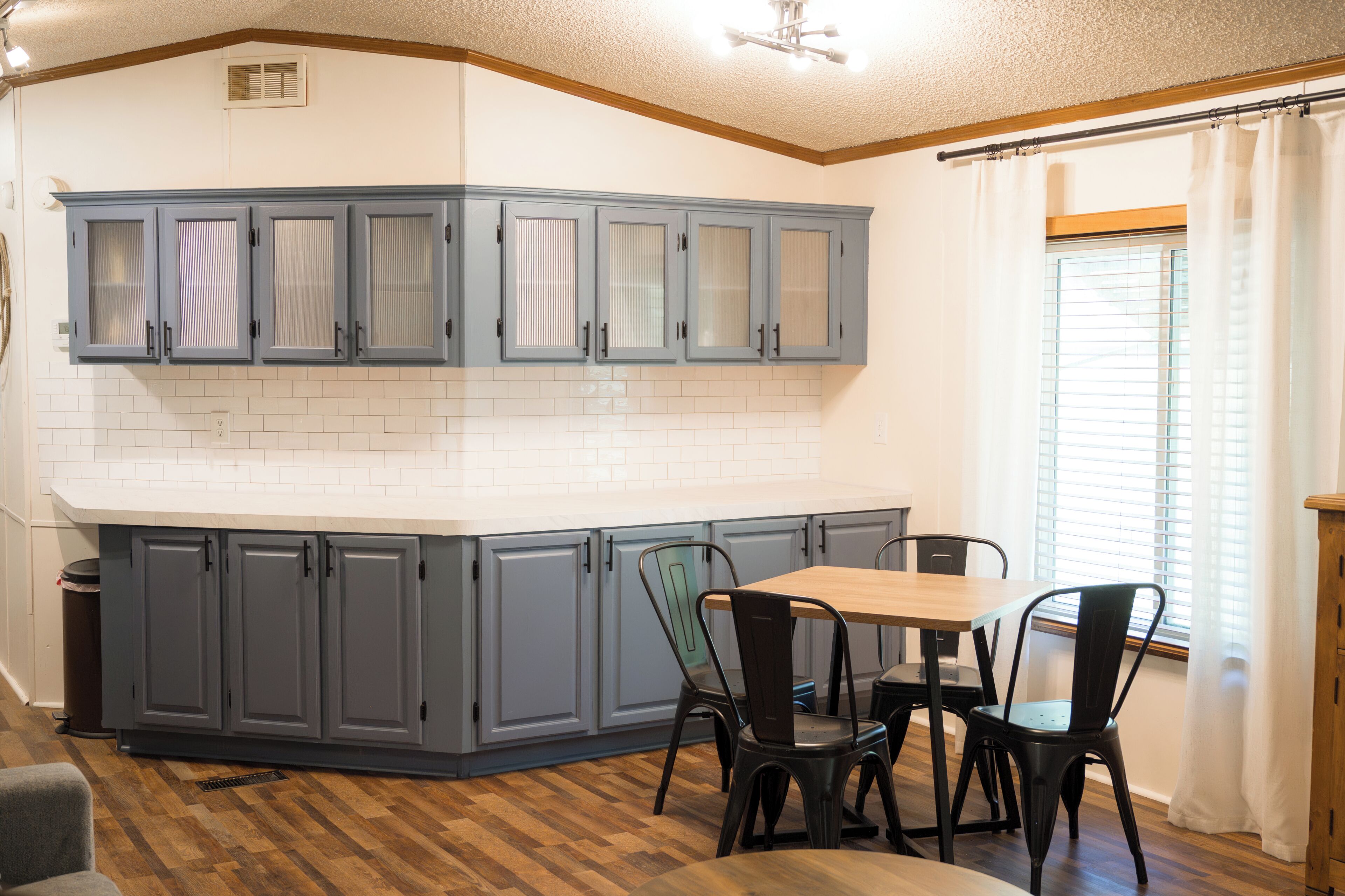 A kitchen with grey cabinets, a white countertop, and a dining area with a table and chairs.