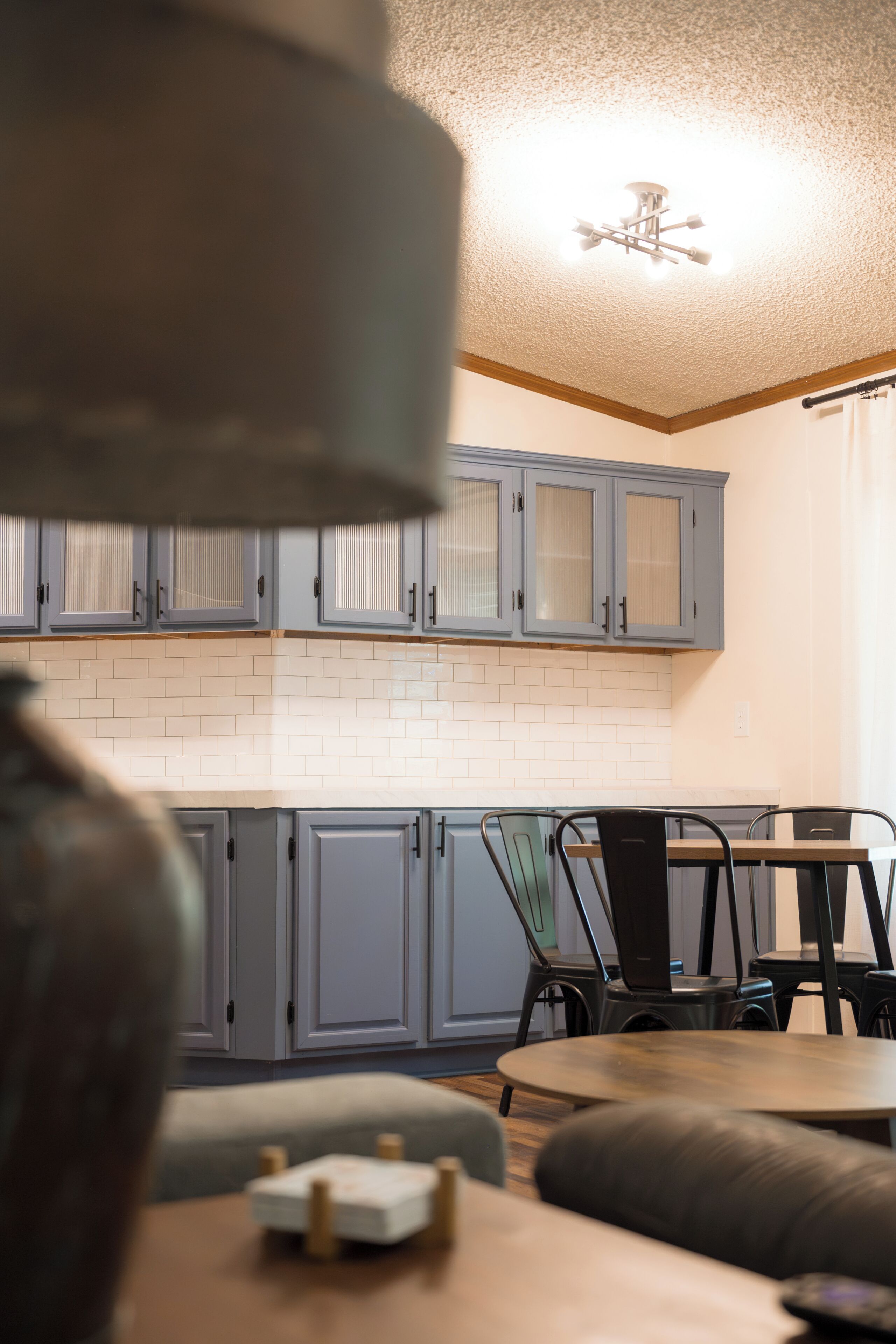 A kitchen with grey cabinets, a white tiled backsplash, and a ceiling fan.