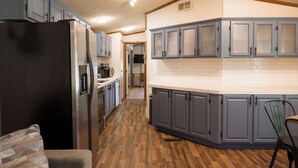 A kitchen with grey cabinets, a black refrigerator, and a wooden floor.