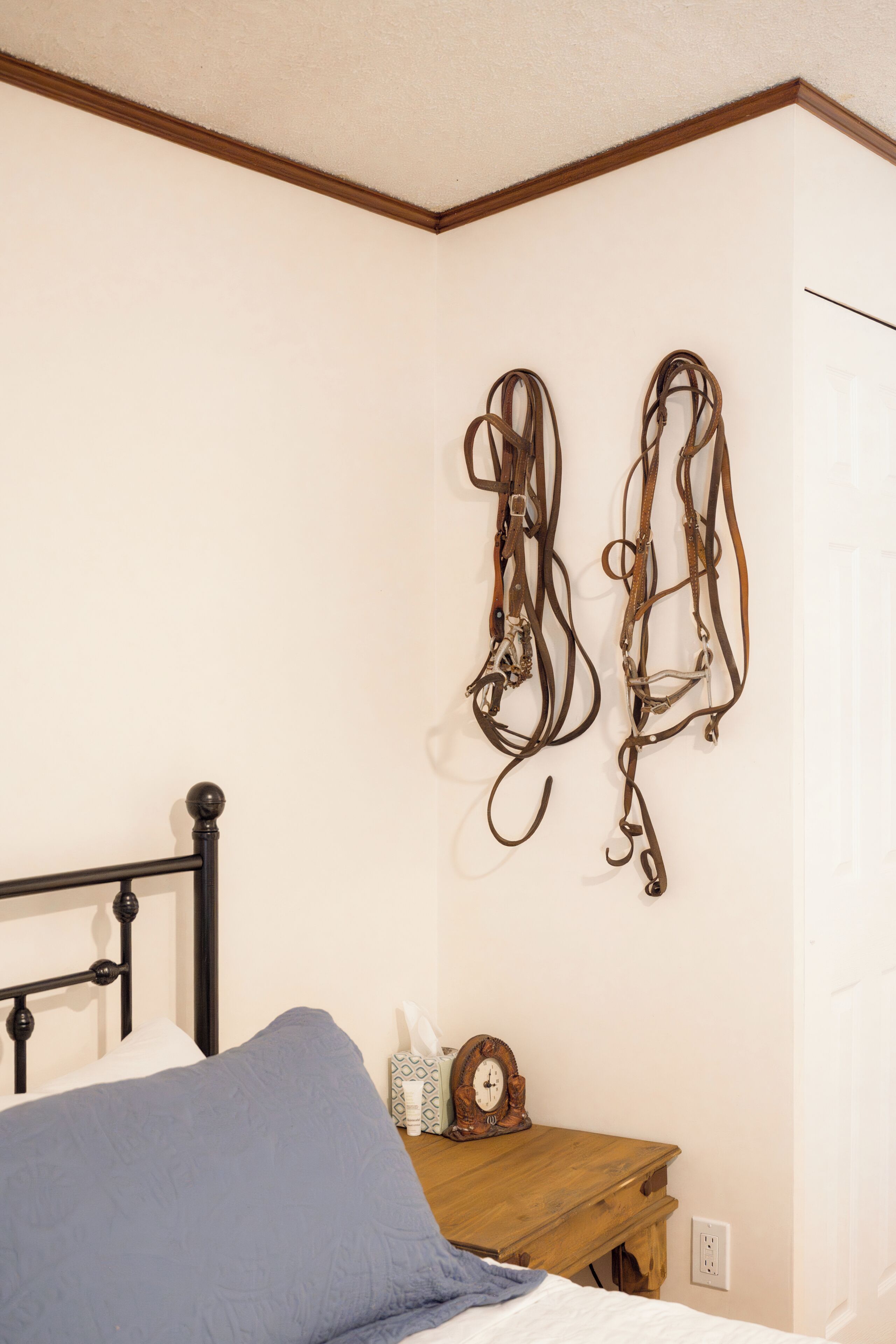A bedroom with a bed, a wooden nightstand, a wall-mounted clock, and two pieces of wall art.