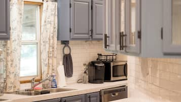 A kitchen with grey cabinets, a stainless steel sink, a coffee maker, and a dish rack.