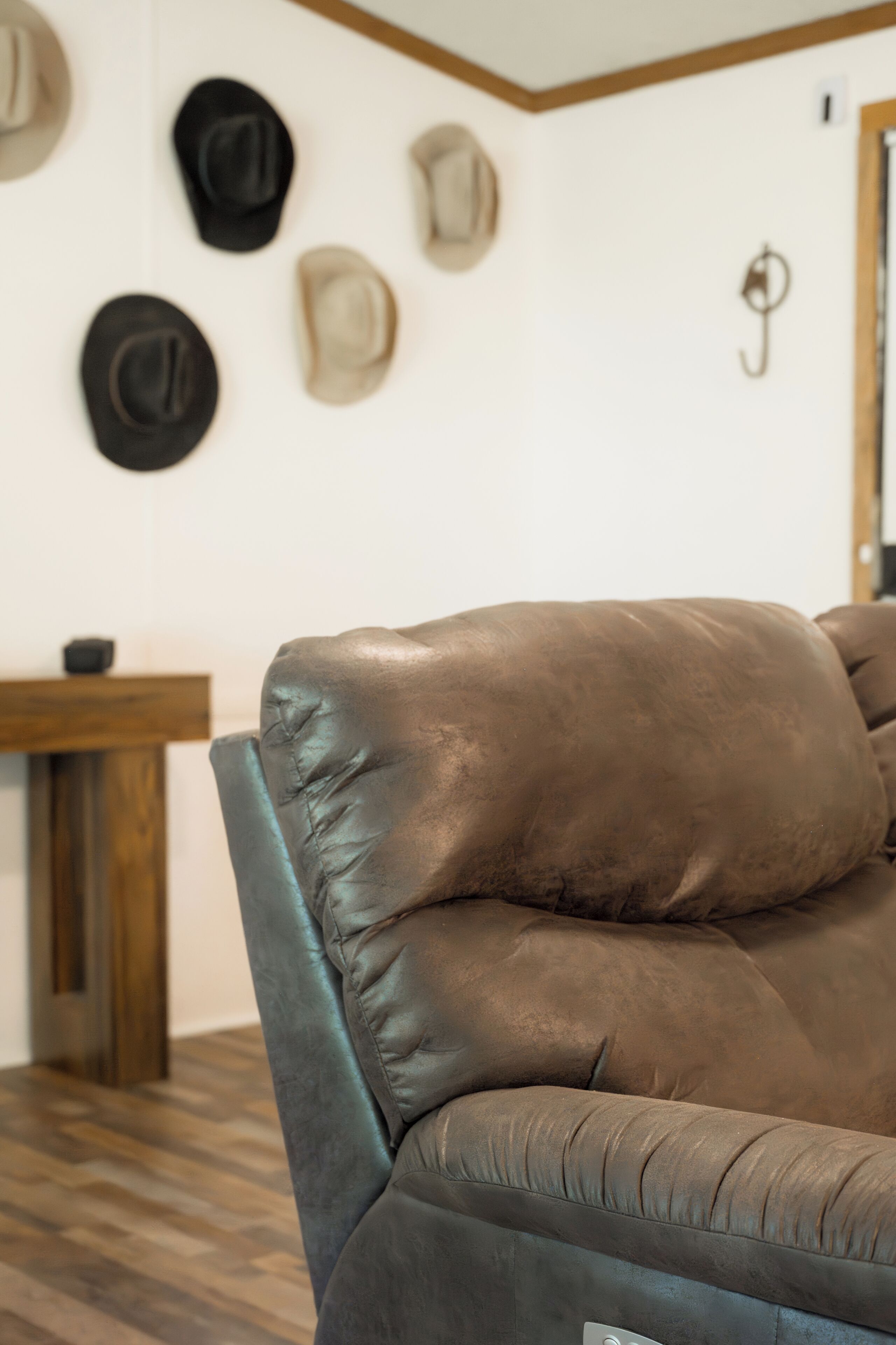 A leather sofa with a wooden frame, a wooden table with a chair, and a wall with several hats hanging.