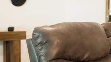 A leather sofa with a wooden frame, a wooden table with a chair, and a wall with several hats hanging.