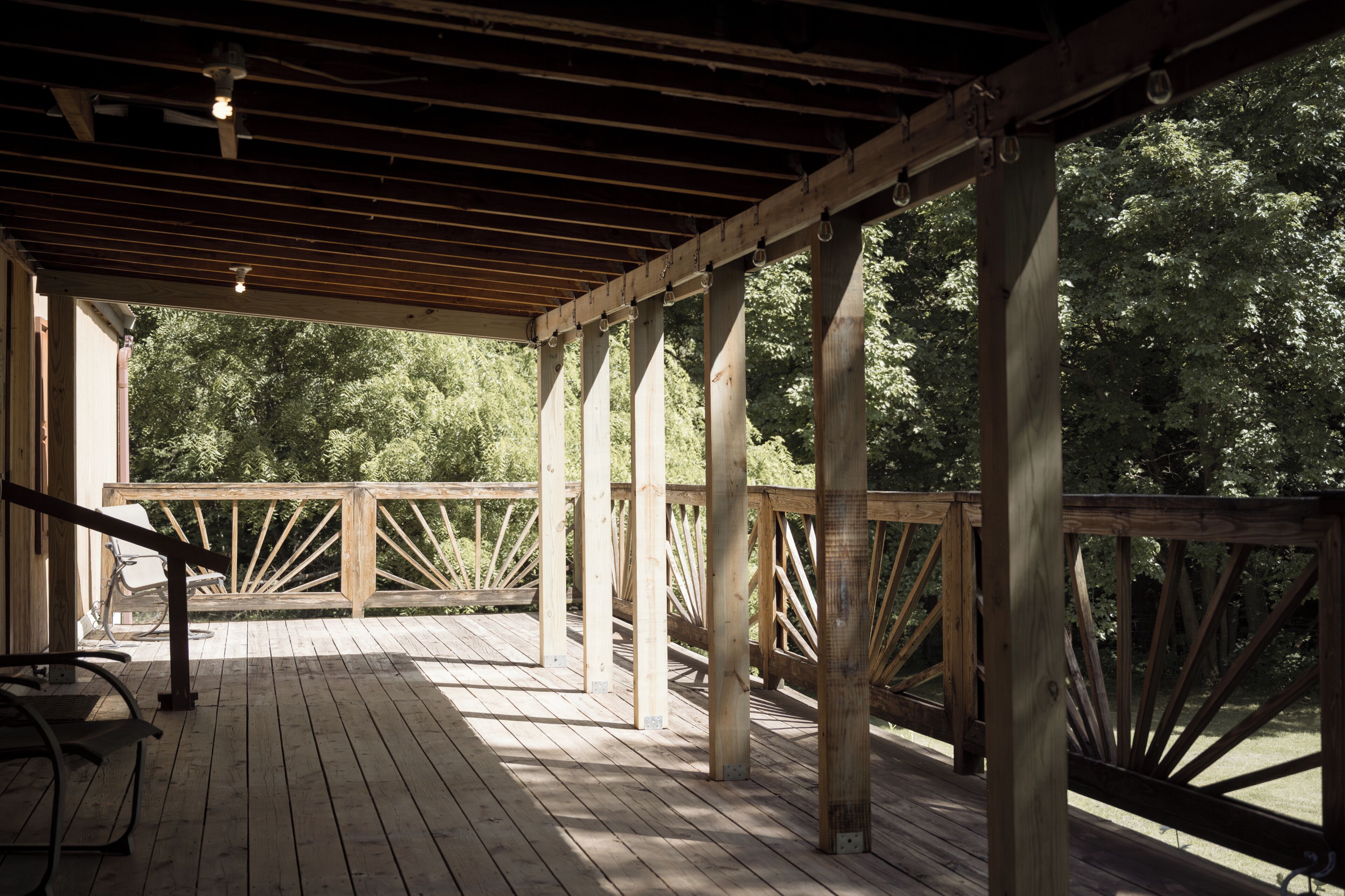 A wooden deck with a railing, a bench, and a view of trees.
