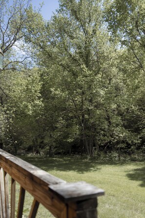 Eine Holzterrasse mit einem Rasenbereich und dichtem Baumbestand im Hintergrund.