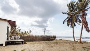 Une maison de plage avec une terrasse, des chaises et un hamac.