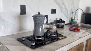 Une cuisine équipée d’une cuisinière à gaz, d’une machine à café, d’un évier et d’une planche à découper avec des légumes.