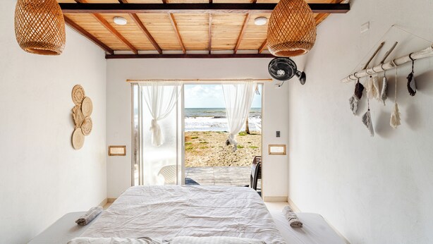 Une chambre avec un lit, une vue sur la plage et un ventilateur de plafond.