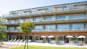 Un hotel de varios pisos con balcones, mobiliario exterior y una piscina.