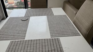 Een kamer met een groot raam, een bank, een tafel met placemats en een stoel.