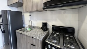 Een kleine keuken met een roestvrijstalen koelkast, een gasfornuis en een koffiezetapparaat.