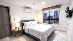Een moderne slaapkamer met een bed, nachtkastjes, een wandtelevisie en uitzicht over de stad.