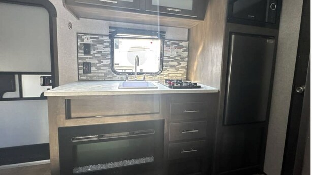 Een compacte keuken met een inbouwmagnetron, een spoelbak en een koelkast.