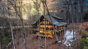 Une cabane à plusieurs niveaux, entourée d’arbres et accessible par un sentier de terre.
