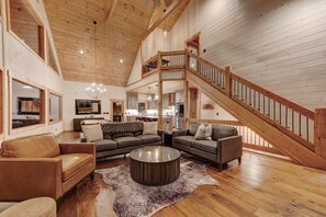 A spacious living area with a wooden staircase, leather sofas, a round coffee table, and a chandelier. - Spacious 4-bedroom mountain view in Ellijay with private hot tub and pool table (Ellijay)