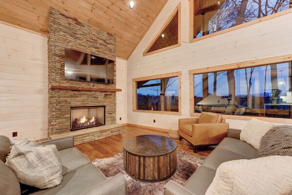 A spacious living room with a stone fireplace, large windows, and modern furniture. - Spacious 4-bedroom mountain view in Ellijay with private hot tub and pool table (Ellijay)