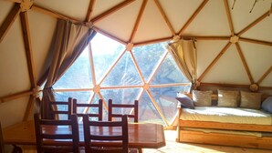 Una habitación en forma de cúpula geométrica con una mesa de madera, sillas y una cama con almohadas.