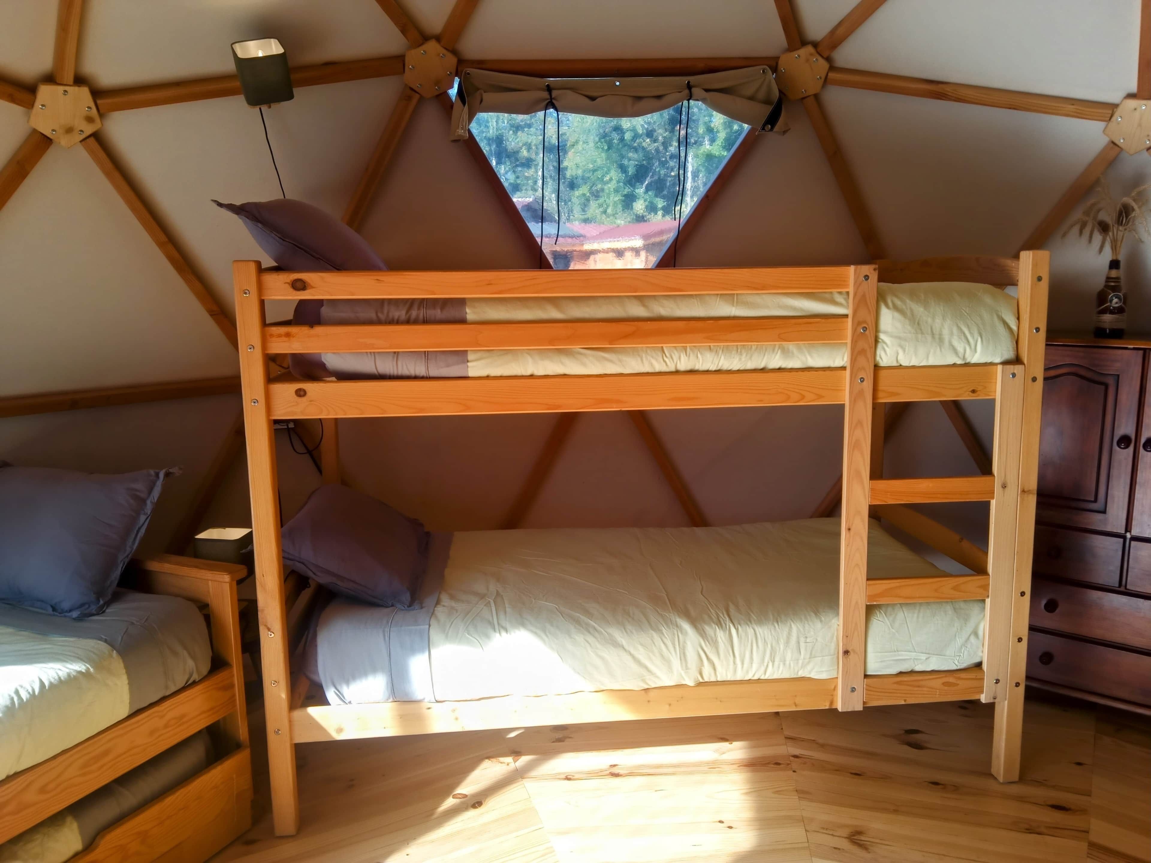 A tent with a bunk bed, a small desk, and a window with a view of trees.