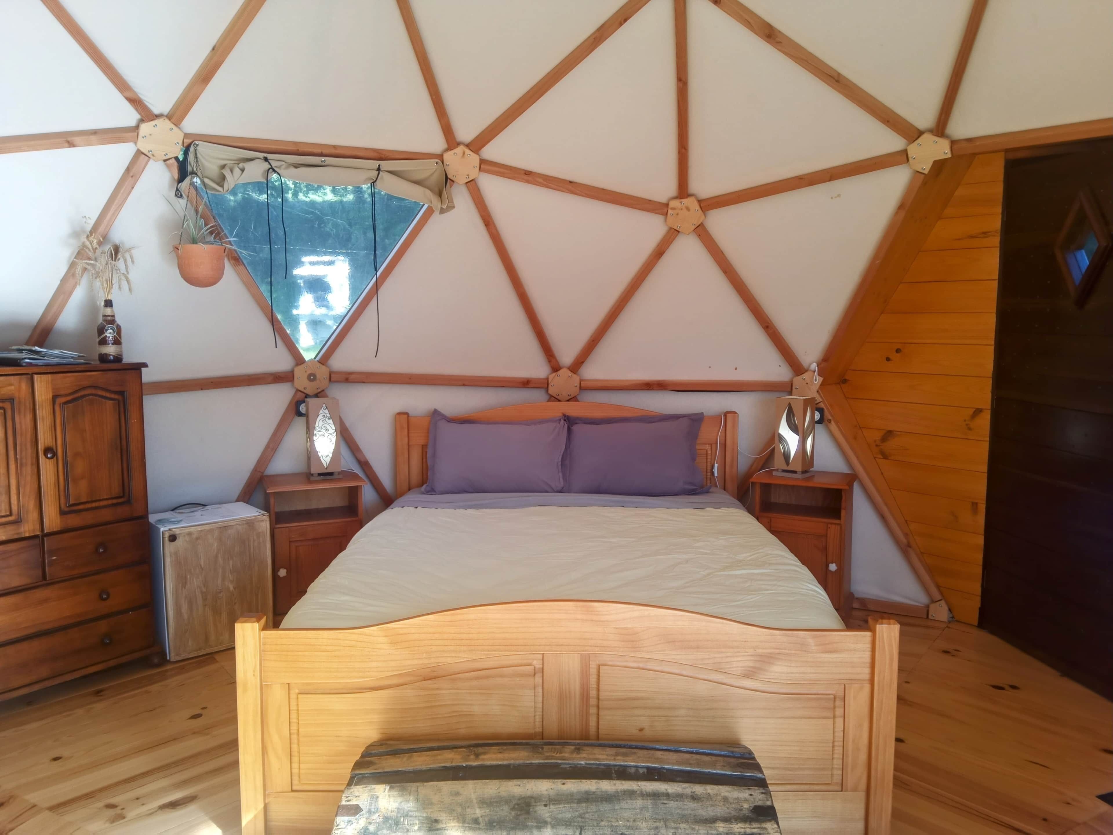 A tent-style room with a bed, wooden cabinets, and a small table.
