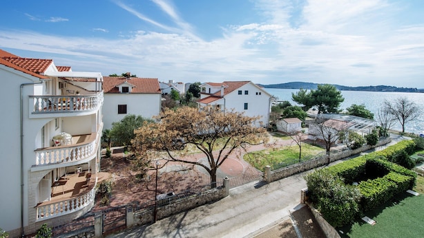 Zona residencial costera con edificios blancos, tejados de tejas rojas y vista al mar.