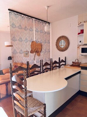 A dining area with a round table, wooden chairs, a decorative wall panel, a hanging light fixture, and a microwave. - Beachfront Getaway with Fantastic Views (L'Ampolla)