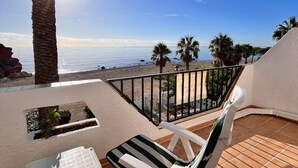 Een balkon met uitzicht op zee, een palmboom en een stoel.