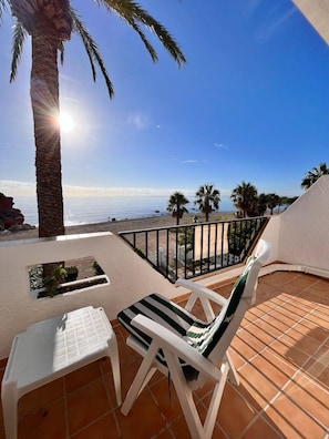 A balcony with a view of the sea, a palm tree, and a chair. - Beachfront Getaway with Fantastic Views (L'Ampolla)