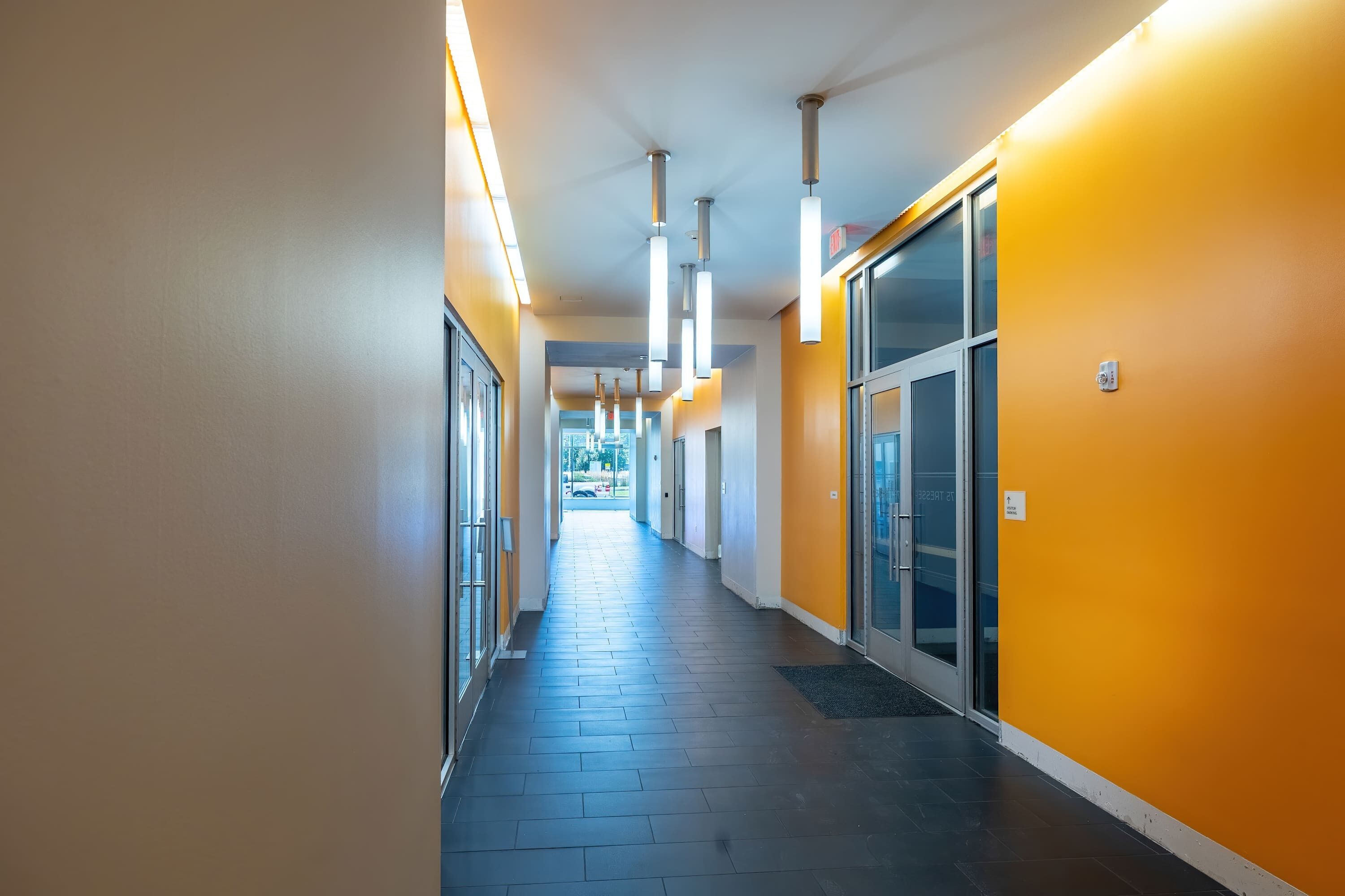 Un couloir doté d’un sol carrelé, de portes en verre et d’un éclairage au plafond.