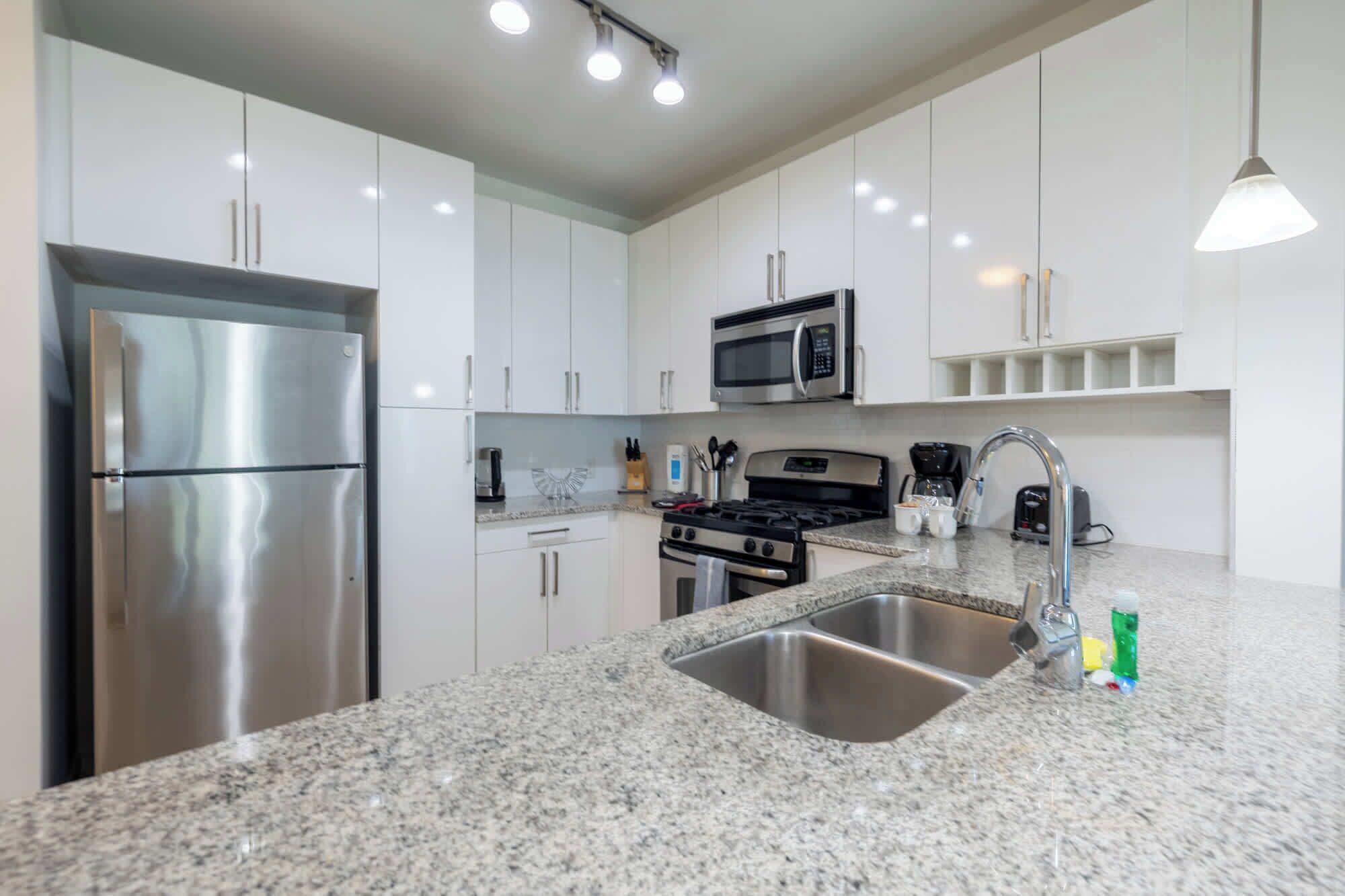 A modern kitchen with stainless steel appliances, granite countertops, and white cabinetry.
