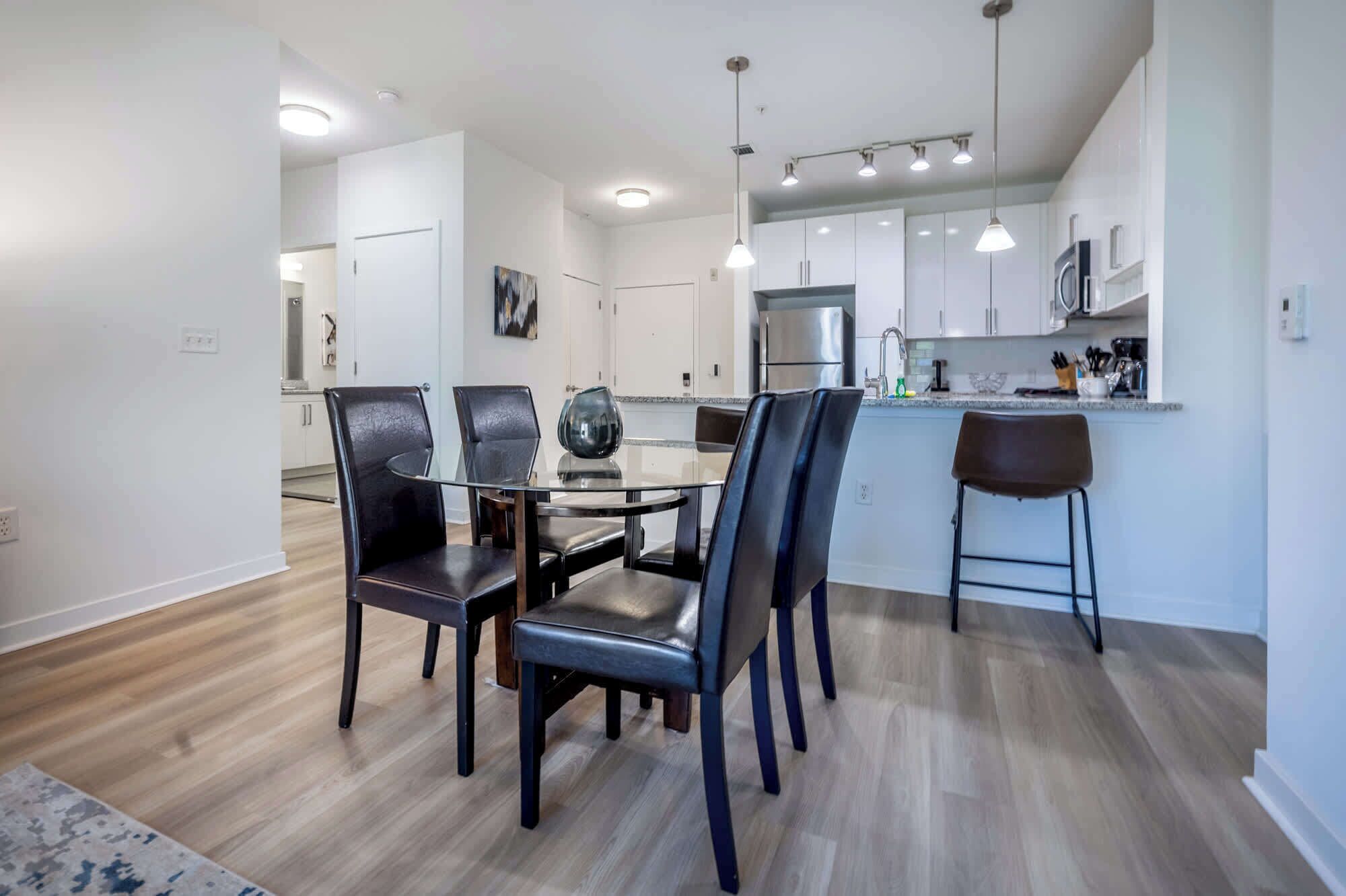 A modern kitchen with white cabinets, a stainless steel refrigerator, and a glass dining table with chairs.