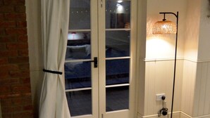 A room with a sliding glass door, a standing floor lamp, a small round table with a remote control, and a patterned rug on the floor. - The Stables in Central Horncastle - Pass the Keys (Horncastle)