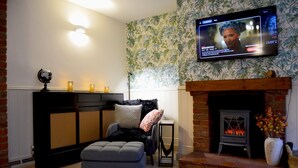 A living room with a fireplace, a television mounted on the wall, a sofa, and a patterned wallpaper. - The Stables in Central Horncastle - Pass the Keys (Horncastle)