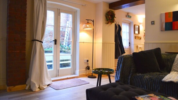 A living room with a sofa, a coffee table, a fireplace, a door with curtains, and a brick wall. - The Stables in Central Horncastle - Pass the Keys (Horncastle)