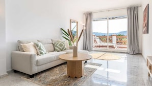 Una sala moderna con sofá, una mesa redonda de madera y vistas a un balcón con mobiliario exterior.