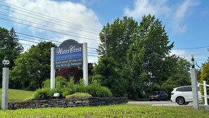 A sign for Water Crest Cottages & Motel with a stone wall and greenery.