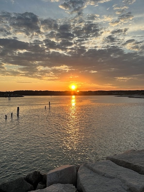 Un coucher de soleil sur une étendue d’eau calme, avec un premier plan rocheux.