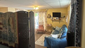 A room with a bed, a chair, a television, and a window with curtains.
