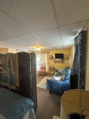 A room with a bed, a chair, a television, and a window with curtains.