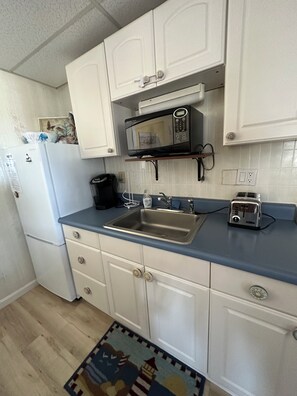 A compact kitchen with white cabinets, a microwave, a toaster, and a sink.