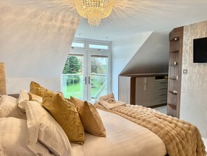 A bedroom with a large bed, a chandelier, a wardrobe, and a view of a green landscape through a glass door. - Luxury Family Home, Near Mumbles with Sea Views - Pass the Keys (Swansea)