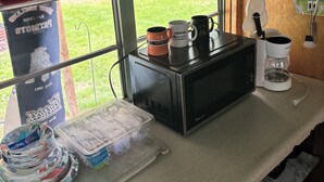 Uma cozinha compacta com micro-ondas, máquina de café e canecas sobre o balcão.