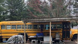 Um autocarro escolar amarelo transformado numa pequena área de estar ao ar livre, com mesas e cadeiras.