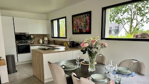 A modern kitchen with white cabinets, a central island, and a dining area with a round table set for four. - Ti Pépin - Contemporary house - 5 min from the beach - Rated 3* furnished for tourism (Fouesnant)