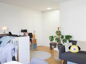 A modern living room with a sofa, a desk with a lamp, a potted plant, and a small stool. - 34m² Paris Studio (Paris)