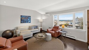 Een moderne woonkamer met een bank, fauteuils, een salontafel en een groot raam met uitzicht op de stad.