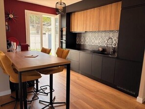A modern kitchen with dark cabinetry, a wooden dining table, and a patterned backsplash. - Villa with large terrace and garden in Angoulins (Angoulins)