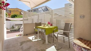En terrasse med et bord dækket til to, et hvidt hegn og udsigt til bygninger i baggrunden.