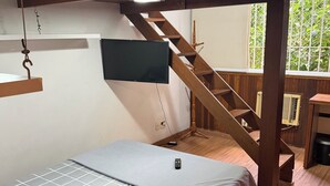Ett rum med en våningssäng, en TV, en trätrappa och ett fönster med utsikt över grönområden.