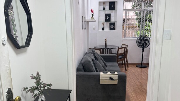 Ett vardagsrum med en soffa, ett litet bord med en vas, en matplats med stolar och en fläkt.